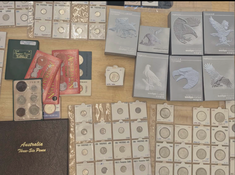 A mixed coin collection laid out on a table: carded pre-decimal coins in album pages, mint sets, an Australia Three-Six Pence album and boxed wedge-tailed eagle coins